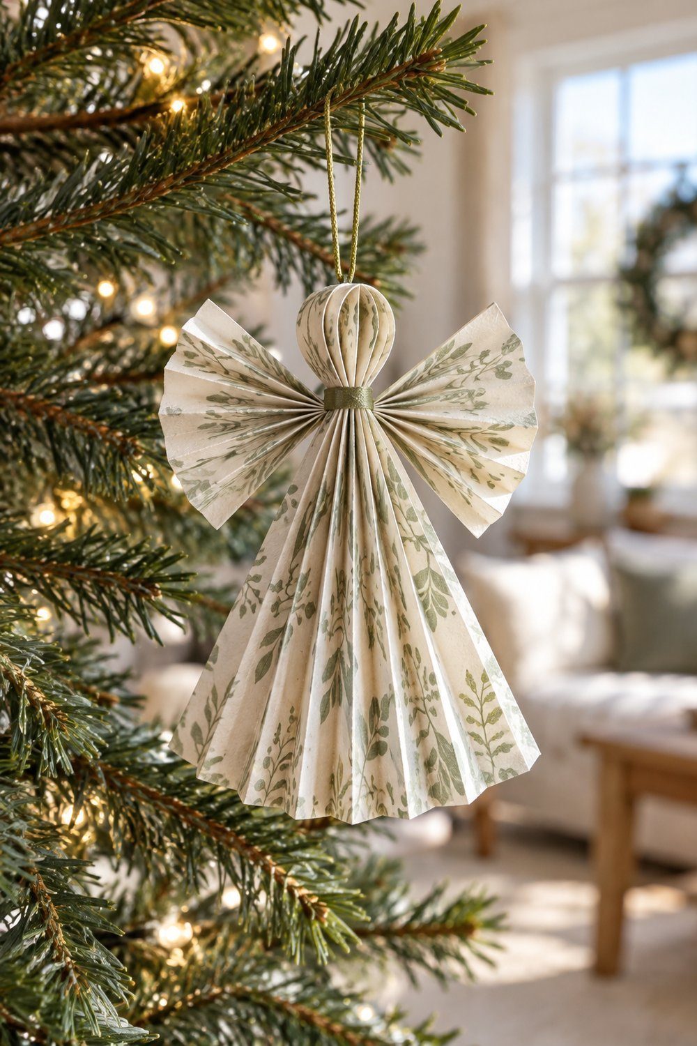 Folded paper angel with pleated skirt and wings hanging on evergreen branches