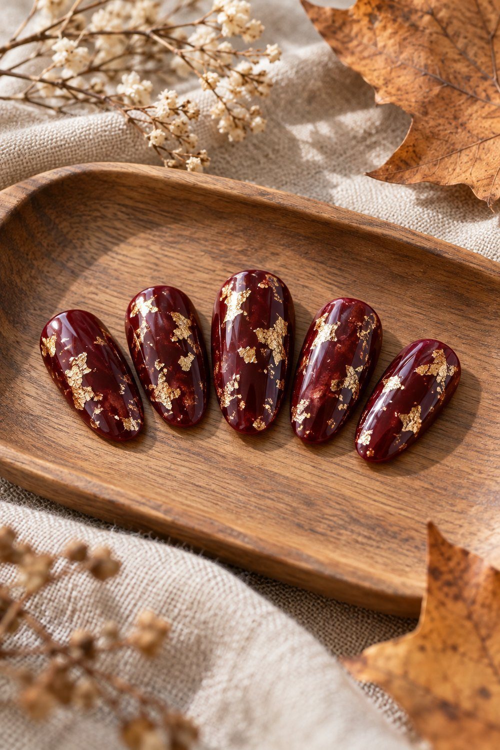 Deep burgundy oval press-on tips scattered with irregular gold leaf