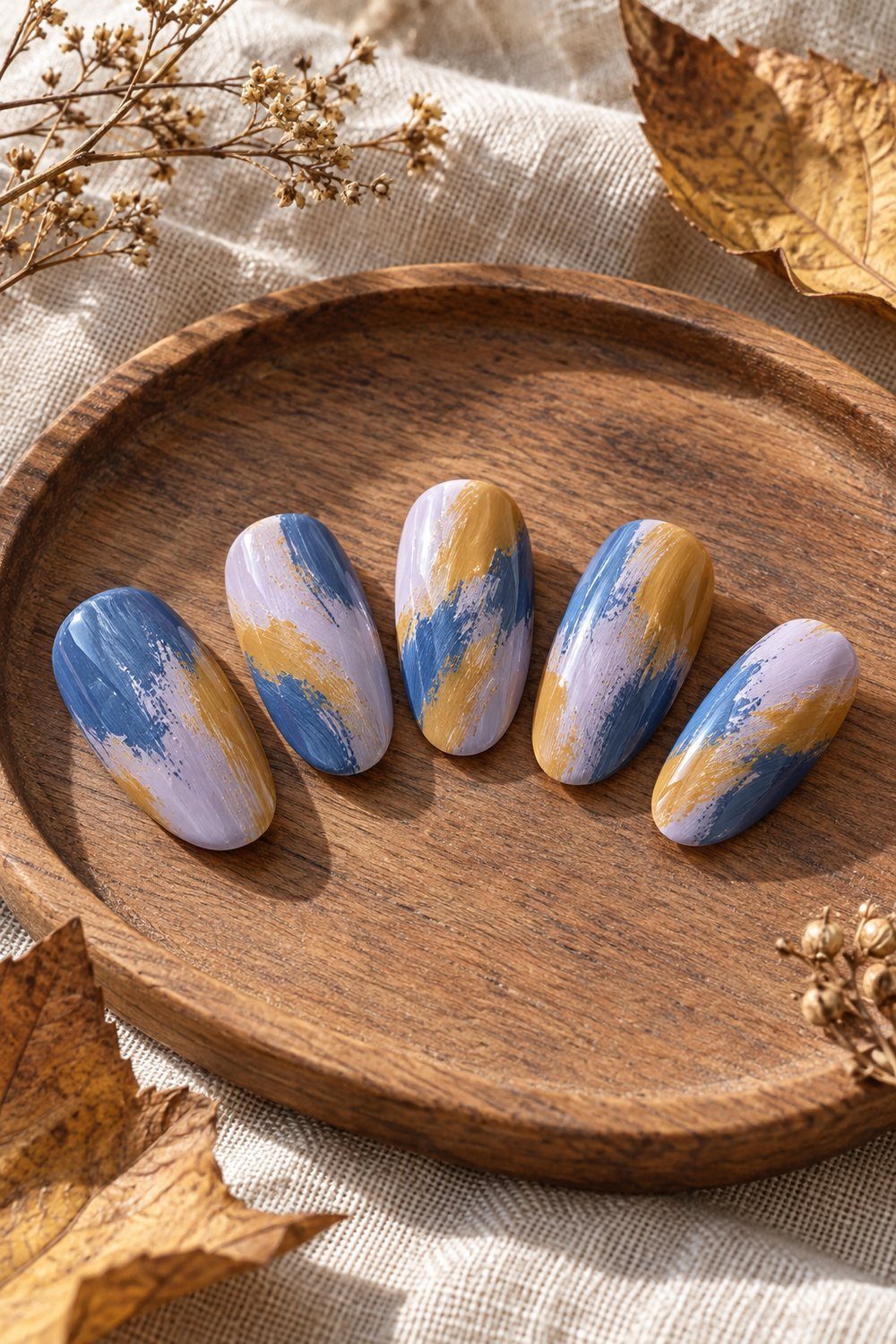 Blue purple and ochre dry-brush swooshes on oval nail swatches