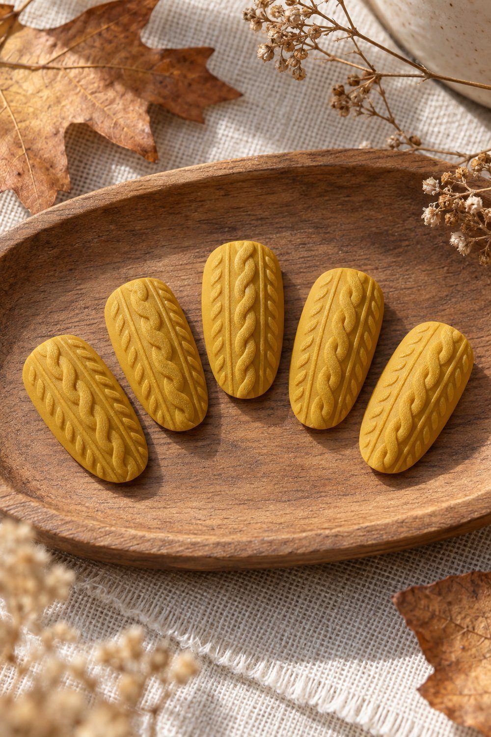 Mustard matte oval nail tips painted with delicate cable-knit stitches