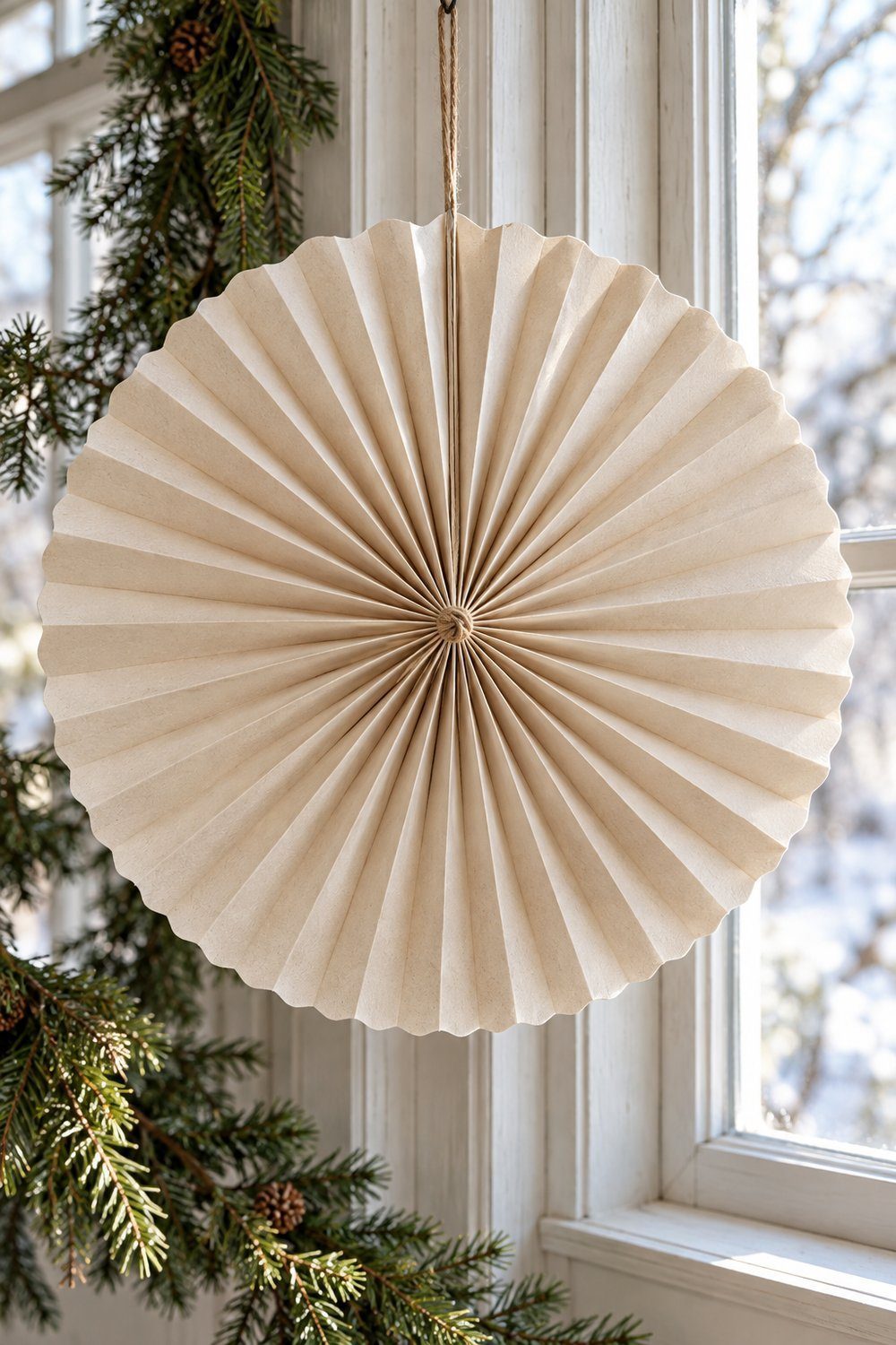 Circular pleated paper rosette hanging beside a farmhouse window at Christmas