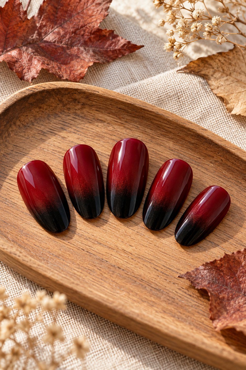 Red and black gradient oval nail tips fanned across natural linen